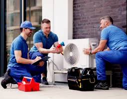 Three HVAC technicians working together beside an outdoor heat pump