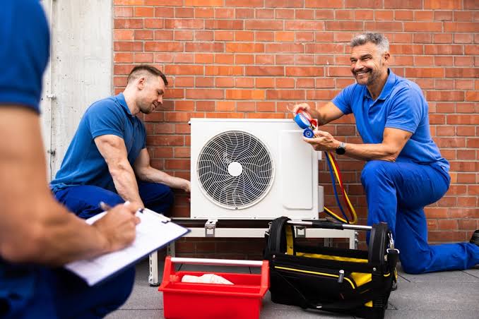 HVAC service team inspecting an outdoor heat pump with pressure gauges