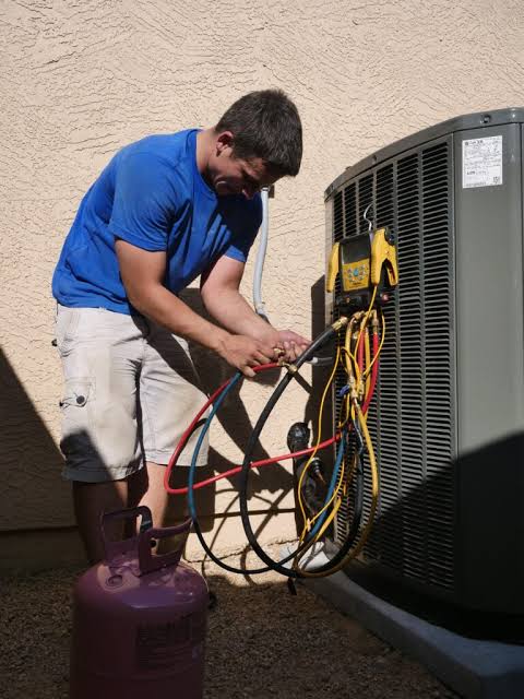 HVAC technician checking service hoses and gauges at a home air conditioner